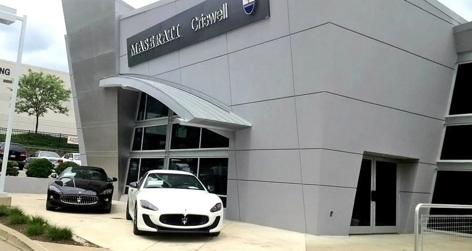 Exterior of a modern Maserati dealership with “Maserati Criswell” signage, featuring a white sports car parked at the entrance and a black car displayed to the side.