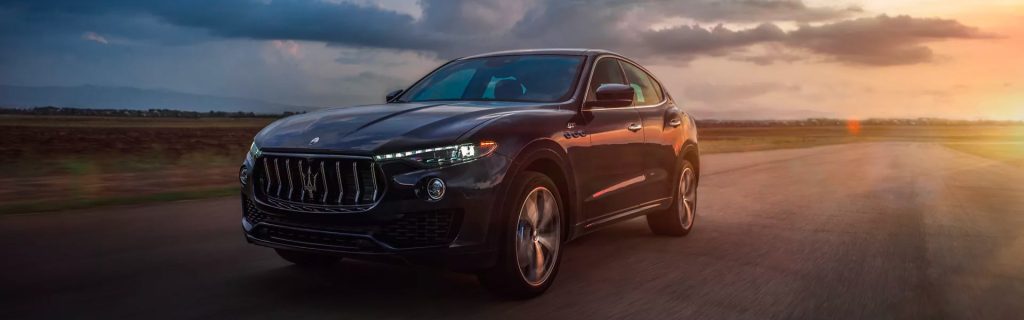 A white Maserati Levante SUV parked on a coastal cliffside overlook, showcasing its front profile against a backdrop of deep blue ocean water.